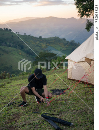 Young man using hammer setting up tent for camping on meadow 78063388