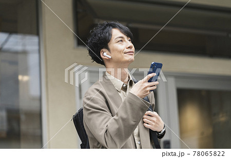 ヘッドホンをしてスマホを持った30代前半の男性 78065822