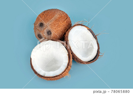 Whole and cracked coconuts on light blue background. De-husked coconut fruits showing the characteristic three pores. Cut in half coconut closeup. 78065880