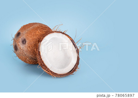 Whole and cracked coconuts on light blue background. De-husked coconut fruits showing the characteristic three pores. Cut in half coconut closeup. 78065897
