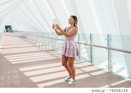 A young woman in a summer dress walks and takes a photo on a tablet A young woman in a summer dress walks and takes a photo on a tablet 78068148