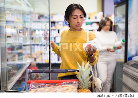 Latina choosing dairy products in fridge at grocery store Latina choosing dairy products in fridge at grocery store 78070563