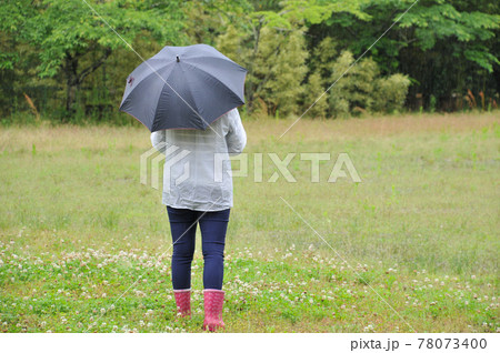 雨の中傘をさし長靴を履いて歩く 78073400
