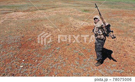 Photo of a soldier sniper in the desert. He stands, looks at the camera and shows his rifle. Photo of a soldier sniper in the desert. He stands, looks at the camera and shows his rifle. 78075006