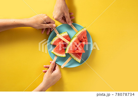 Hand picking up watermelon slices popsicles on blue plate Hand picking up watermelon slices popsicles on blue plate 78078734