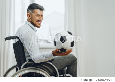 Young man in wheelchair holding football ball Young man in wheelchair holding football ball 78082451