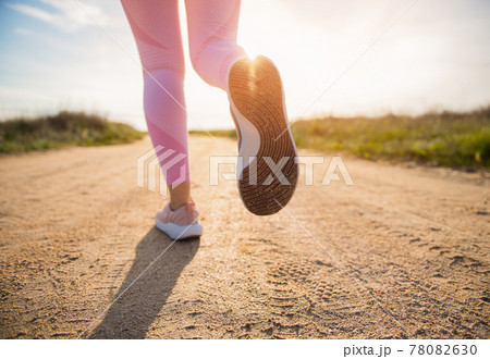 Closeup of female athlete running on empty country steppe road at sunset Closeup of female athlete running on empty country steppe road at sunset 78082630