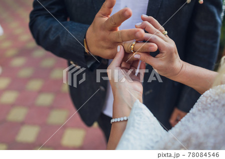 Bride putting a wedding ring on groom's finger. 78084546