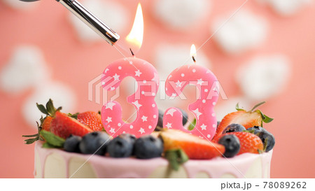 Birthday cake number 33, pink candle on beautiful cake with berries and lighter with fire against background of white clouds and pink sky. Close-up Birthday cake number 33, pink candle on beautiful cake with berries and lighter with fire against background of white clouds and pink sky. Close-up 78089262