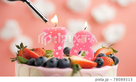 Birthday cake number 78, pink candle on beautiful cake with berries and lighter with fire against background of white clouds and pink sky. Close-up Birthday cake number 78, pink candle on beautiful cake with berries and lighter with fire against background of white clouds and pink sky. Close-up 78089313