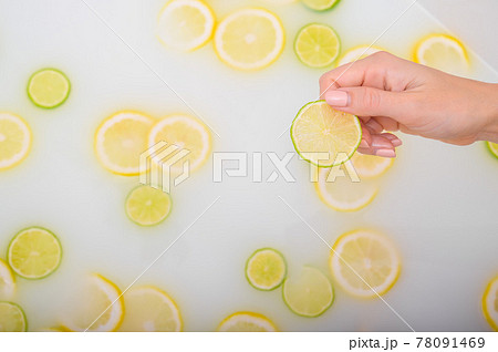 Close-up of a female hand holding a slice of citrus fruit in a milk bath. Close-up of a female hand holding a slice of citrus fruit in a milk bath. 78091469
