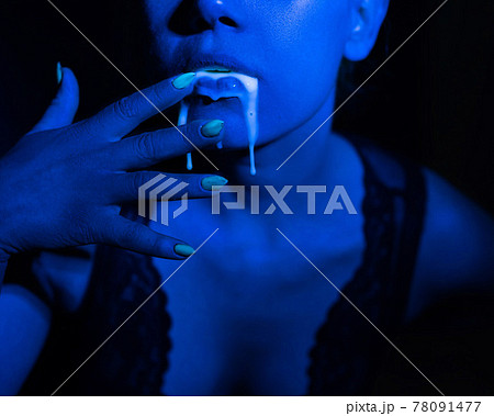 A thick white liquid flows down the lips of a young European girl. Dripping down. Ultraviolet, blue light. Close-up portrait. Spit out. A thick white liquid flows down the lips of a young European girl. Dripping down. Ultraviolet, blue light. Close-up portrait. Spit out. 78091477
