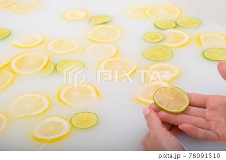 Close-up of a female hand holding a slice of citrus fruit in a milk bath. 78091510
