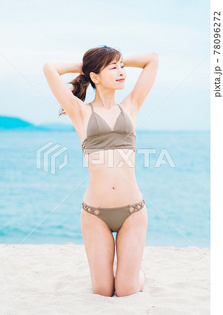 砂浜で膝立ちする水着の女性 78096272