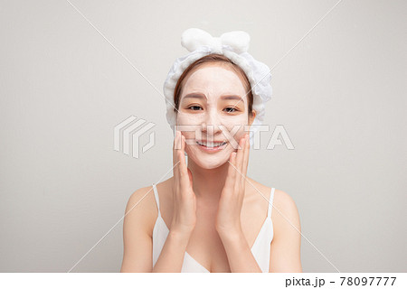 Portrait of confident lady in bathrobe and towel on head with joy while touching her face with clay mask while using anti-aging procedures 78097777
