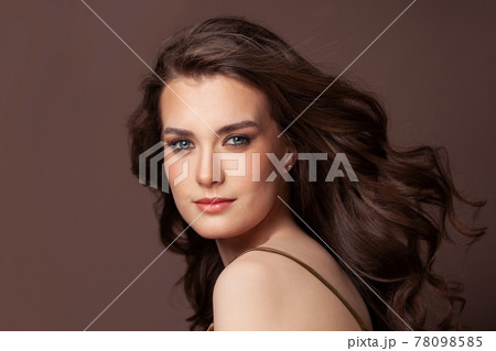 Portrait of cheerful woman brunette with clear skin and healthy curly hairstyle on brown background 78098585