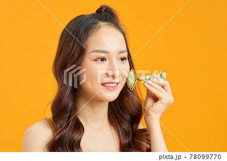 Beautiful Asian woman uses jade roller to massage her face Beautiful Asian woman uses jade roller to massage her face 78099770