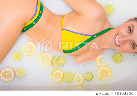 Beautiful redhead woman takes a milk bath with lemon and lime slices. Skin care and whitening. A girl in a yellow-green bikini does the Cleopatra rejuvenation procedure. Beautiful redhead woman takes a milk bath with lemon and lime slices. Skin care and whitening. A girl in a yellow-green bikini does the Cleopatra rejuvenation procedure. 78103250