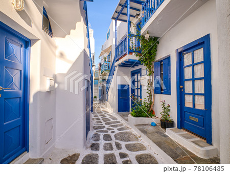 Beautiful traditional narrow alleyways of Greek island towns. White houses, flower pots, blue balconies and doors. Mykonos, Greece 78106485