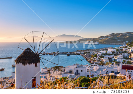 Beautiful view of Greek white windmill overlooking Mykonos, Greece at sunset. Bay, boats, cruise liner, whitewashed houses, islands, hazy background. 78108253