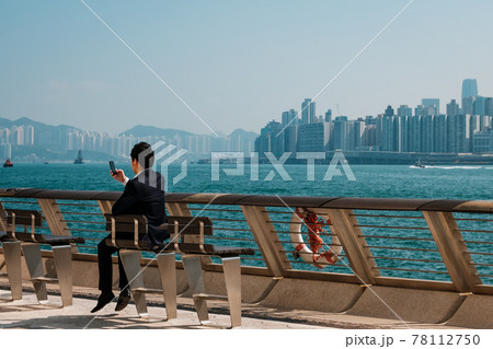 Businessman looking at smart mobile phone outdoors with skyline background, Hong Kong - Businessman looking at smart mobile phone outdoors with skyline background, Hong Kong - 78112750