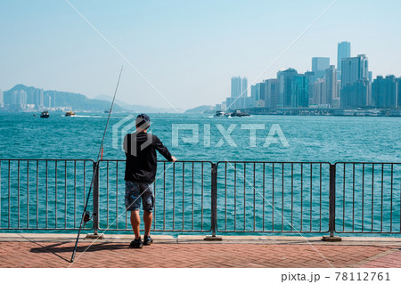 fisher man with fishing rod on coast with skyline of Hong Kong, Kowloon 78112761