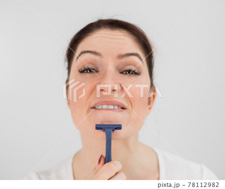 Caucasian funny woman shaves her face with a straight razor on a white background. Copy space. 78112982