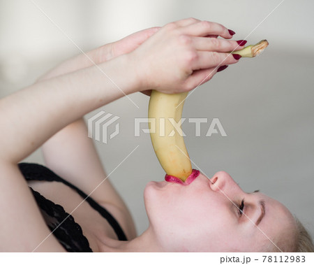 The blonde in black lace underwear erotically eats a banana. Attractive woman with sensual red lips sexually sucks and licks a banana. Oral pleasure. 78112983