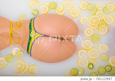 Beautiful woman takes a milk bath with lemon and lime slices. Skin Care & Whitening. Unrecognizable Girl in a Yellow-Green Bikini 78112997