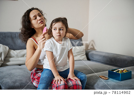 Adorable girl sitting on her mother's legs while she is combing her hair 78114902