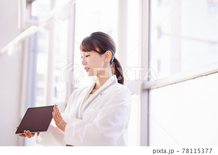 フレーム外の人物にタブレット端末の画面を見せる医療従事者の女性 78115377