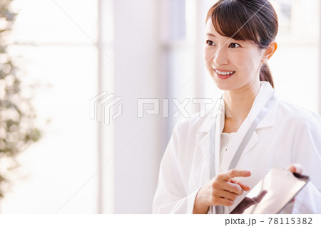 フレーム外の人物にタブレット端末の画面を見せる医療従事者の女性 78115382
