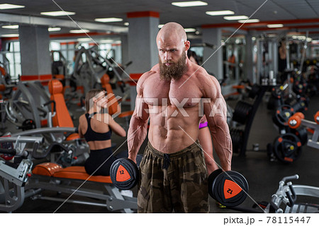 A bearded man and a group of women are engaged in the gym with dumbbells. The bodybuilder does exercises for biceps and triceps. A lesson from a personal trainer. 78115447