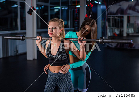 Young athletic girl doing barbell squats in the gym under the supervision of a trainer. A female coach teaches a ward to squat with a bar. Personal training. Exercises on the buttocks. Young athletic girl doing barbell squats in the gym under the supervision of a trainer. A female coach teaches a ward to squat with a bar. Personal training. Exercises on the buttocks. 78115485