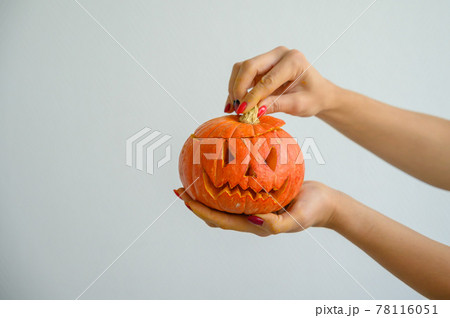 Female hands holding a pumpkin for Halloween. Close-up of a woman opens the jack-o'-lantern cover on a white background on the eve of all the saints. front view. Female hands holding a pumpkin for Halloween. Close-up of a woman opens the jack-o'-lantern cover on a white background on the eve of all the saints. front view. 78116051
