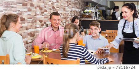 attractive brunette waitress serving family in family cafe 78116724