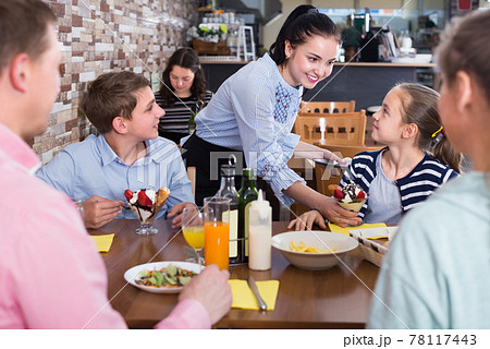 Polite attentive waitress serving dishes to family Polite attentive waitress serving dishes to family 78117443