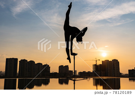 Flexible female circus Artist keep balance on one hand on the rooftop against dramatic sunset and cityscape. Handstand and equilibrium concept Flexible female circus Artist keep balance on one hand on the rooftop against dramatic sunset and cityscape. Handstand and equilibrium concept 78120189