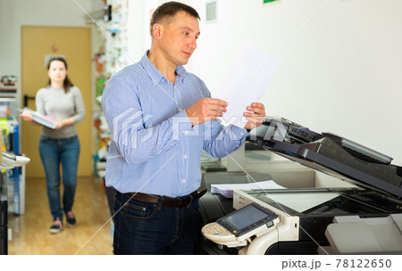 Confident businessman using printer in office Confident businessman using printer in office 78122650