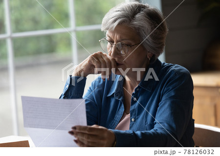Middle aged female reading letter looking concerned 78126032