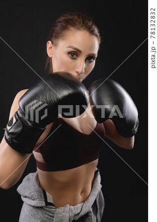 Portrait Caucasian fitness girl in boxing gloves stands in a rack on a black background, portrait of a strong and independent woman fighter 78132832