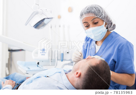 Female dentist in face mask with male patient Female dentist in face mask with male patient 78135963