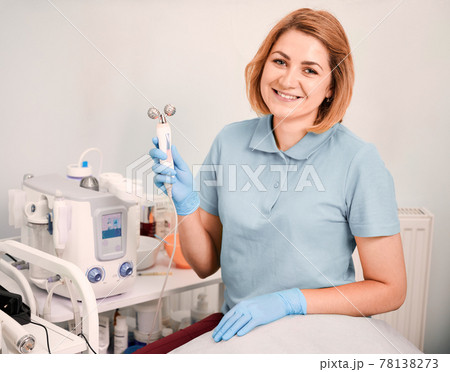 Cheerful female beautician holding facial roller. 78138273