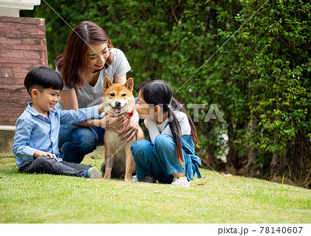 Asian mother and two kids sitting and playing together with Shiba inu dog in public park Asian mother and two kids sitting and playing together with Shiba inu dog in public park 78140607