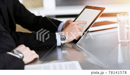 Businessman using tablet computer and work together with his colleague in sunny modern office, close-up. Unknown business people at meeting. Teamwork and partnership concept Businessman using tablet computer and work together with his colleague in sunny modern office, close-up. Unknown business people at meeting. Teamwork and partnership concept 78141578