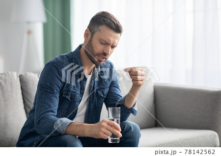 Bearded man in pain with glass of water taking medicine Bearded man in pain with glass of water taking medicine 78142562