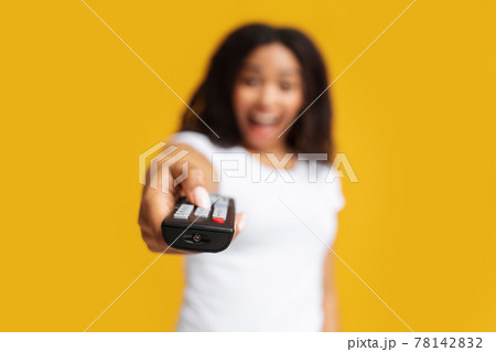 Happy african american woman pointing remote controller to camera over yellow studio background, selective focus Happy african american woman pointing remote controller to camera over yellow studio background, selective focus 78142832