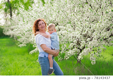 mother holds her young son in a flowering spring garden. parental love and care 78143437