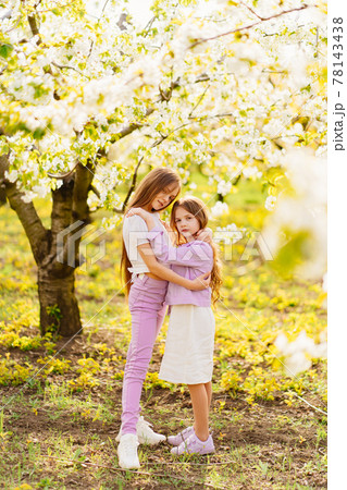 two girls sisters have fun and cuddle in the garden with flowering trees. two girls sisters have fun and cuddle in the garden with flowering trees. 78143438