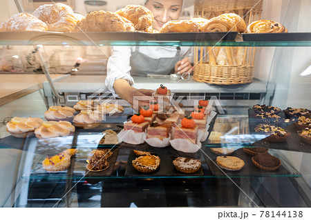 Confectioner shot through glass display in her shop 78144138